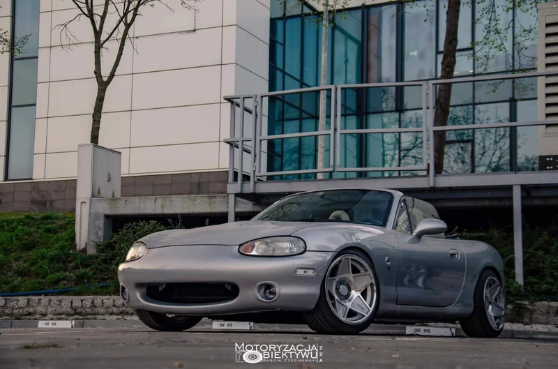 Srebrna Mazda MX-5 NB przed nowoczesnym budynkiem